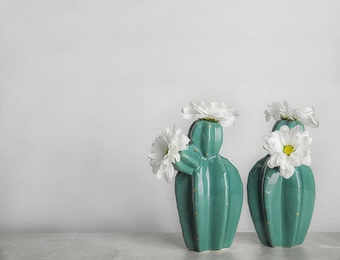 Trendy cactus shaped vases with flowers on table against light wall. Creative decor