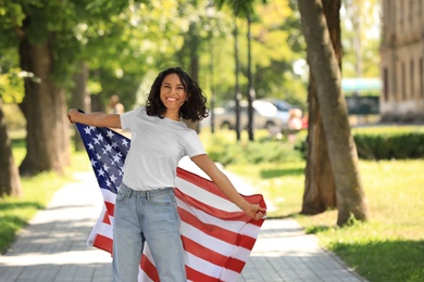 Happy young woman with American flag on sunny day