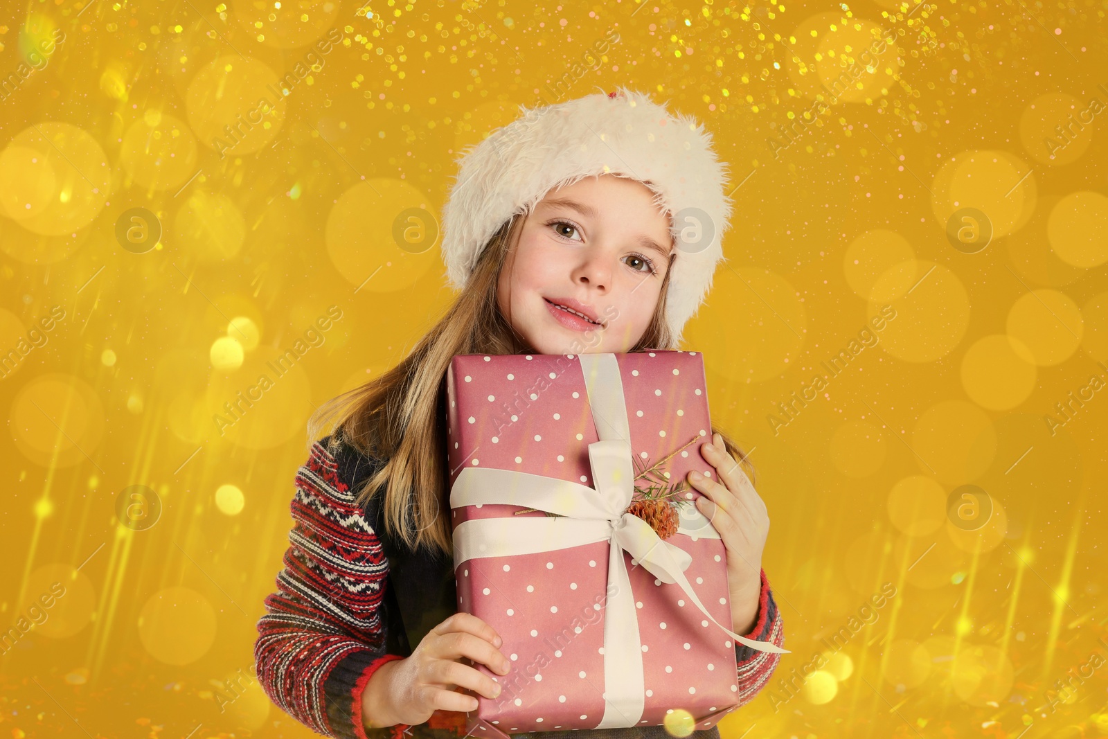 Image of Cute child in Santa hat with Christmas gift on yellow background