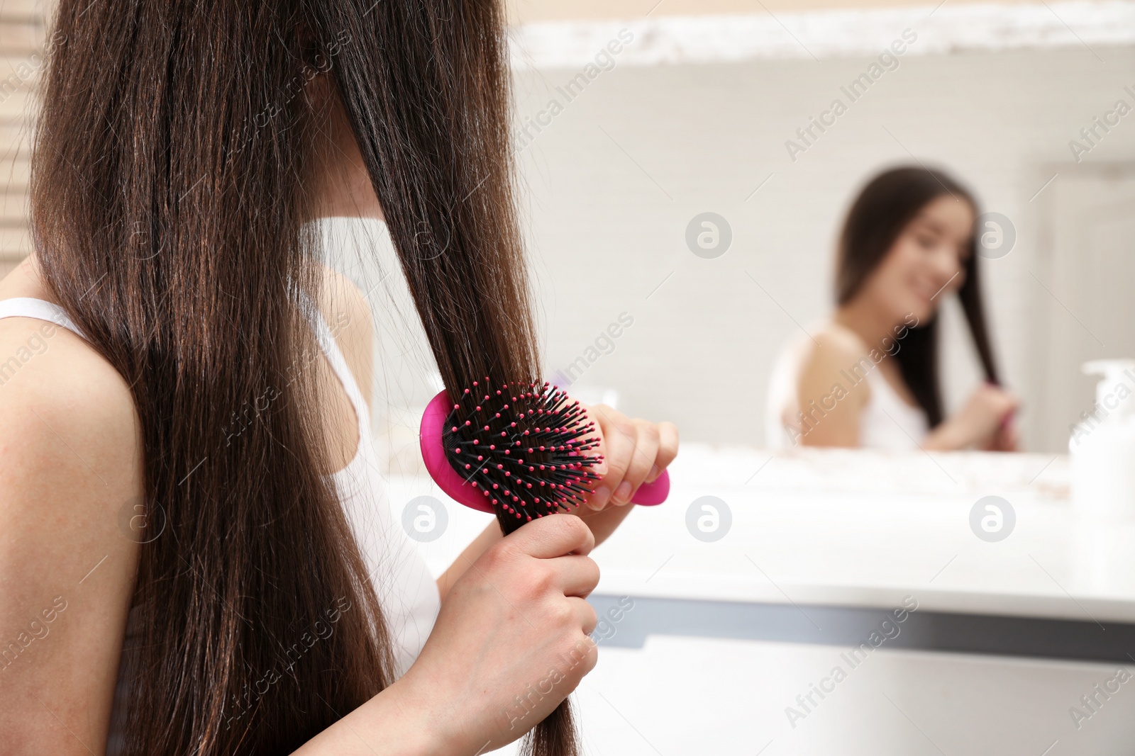 Photo of Beautiful young woman with hair brush near mirror in bathroom