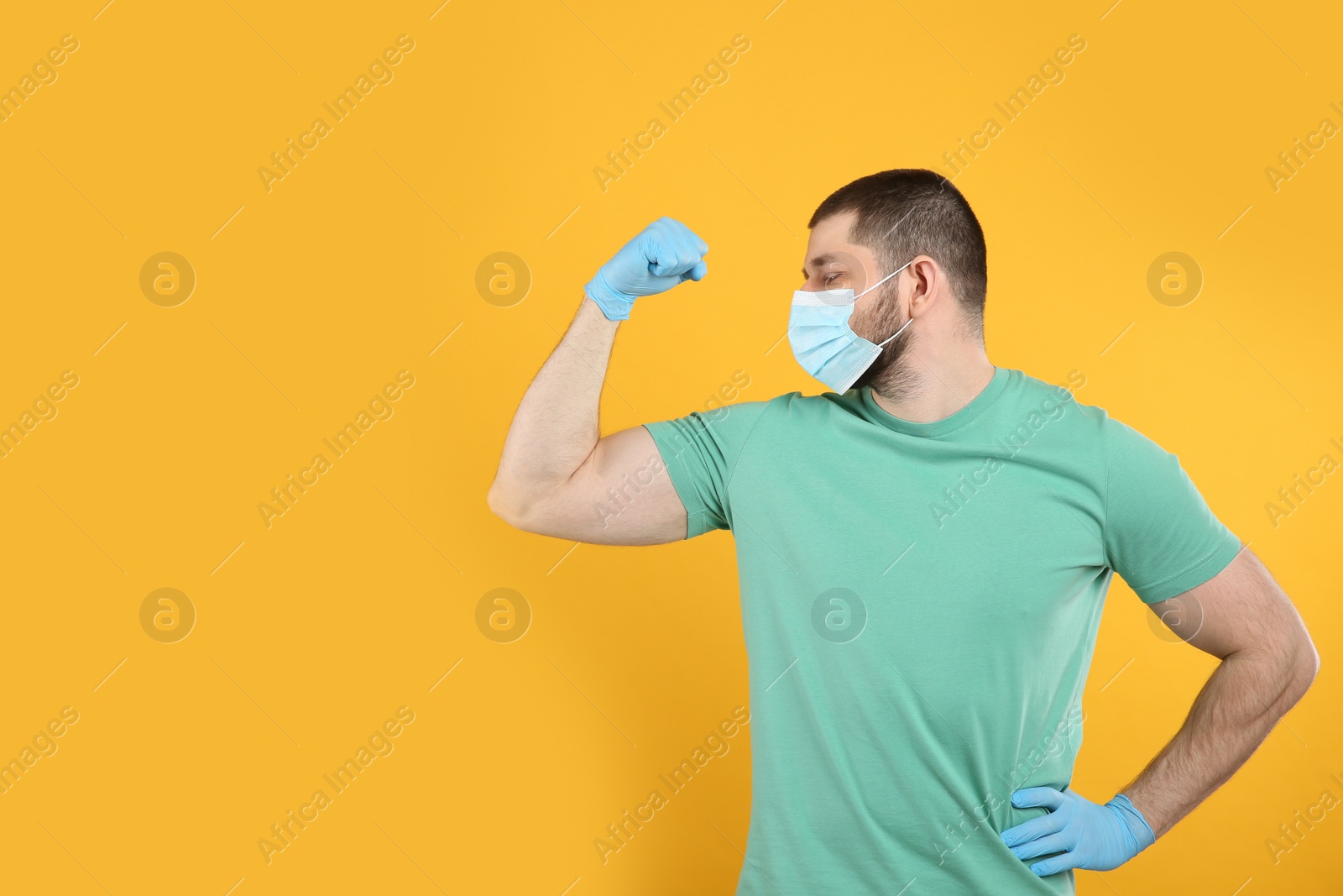 Photo of Man with protective mask and gloves showing muscles on yellow background, space for text. Strong immunity concept