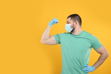 Man with protective mask and gloves showing muscles on yellow background, space for text. Strong immunity concept