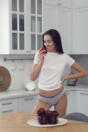 Photo of Young woman with apple in white t-shirt and comfortable underwear indoors
