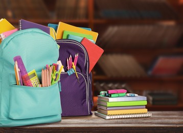 Backpacks with school stationery on wooden table in library, space for text