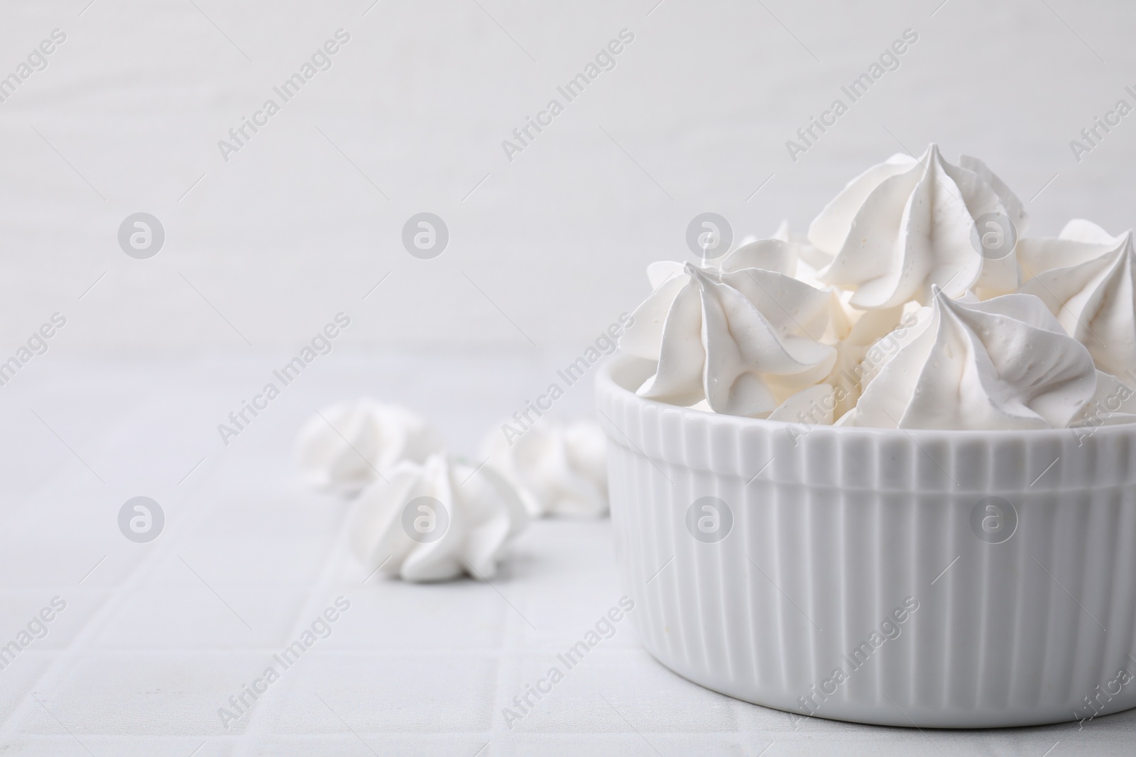 Photo of Delicious meringue cookies in bowl on white tiled table, closeup. Space for text