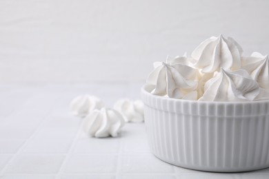 Photo of Delicious meringue cookies in bowl on white tiled table, closeup. Space for text