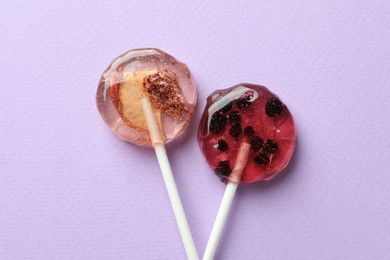 Photo of Sweet colorful lollipops with berries on lilac background, flat lay