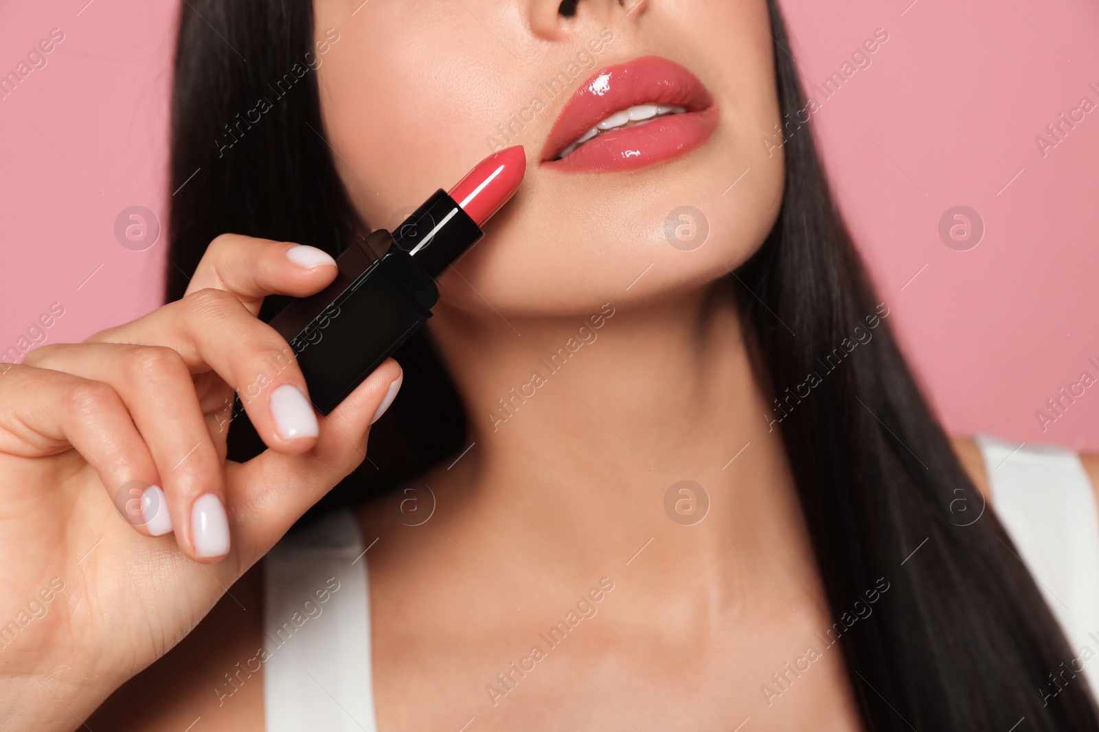 Photo of Young woman with beautiful makeup holding glossy lipstick on pink background, closeup