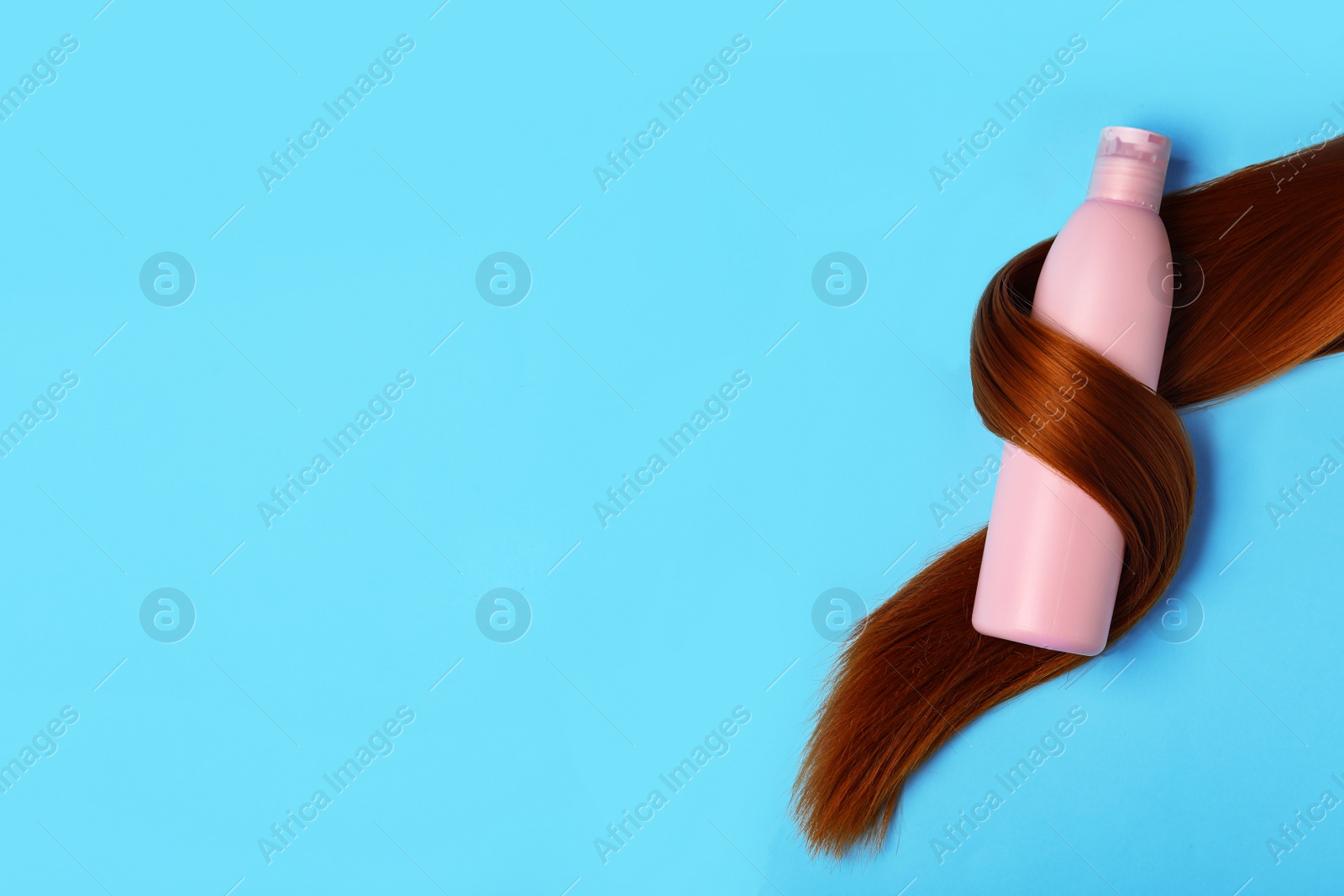 Photo of Shampoo bottle wrapped in lock of hair on light blue background, flat lay with space for text. Natural cosmetic products