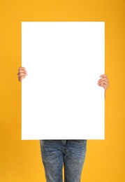 Photo of Man holding white blank poster on yellow background. Mockup for design