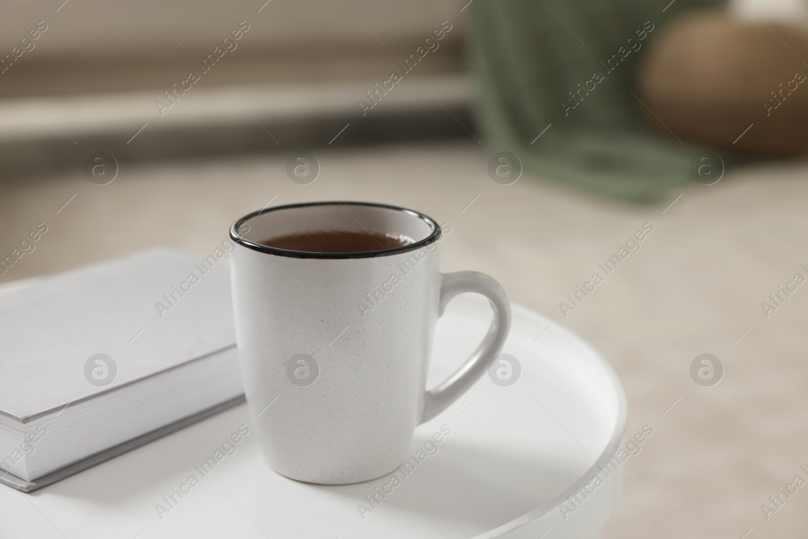 Photo of Ceramic mug of tea and book on white table indoors. Mockup for design