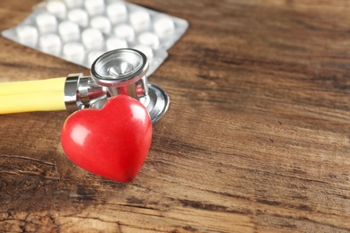 Photo of Stethoscope, pills and small red heart on wooden table. Heart attack concept