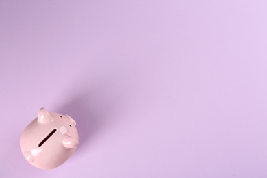 Photo of Piggy bank on violet background, top view. Space for text