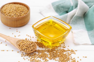 Photo of Bowl of natural oil and mustard seeds on white wooden table