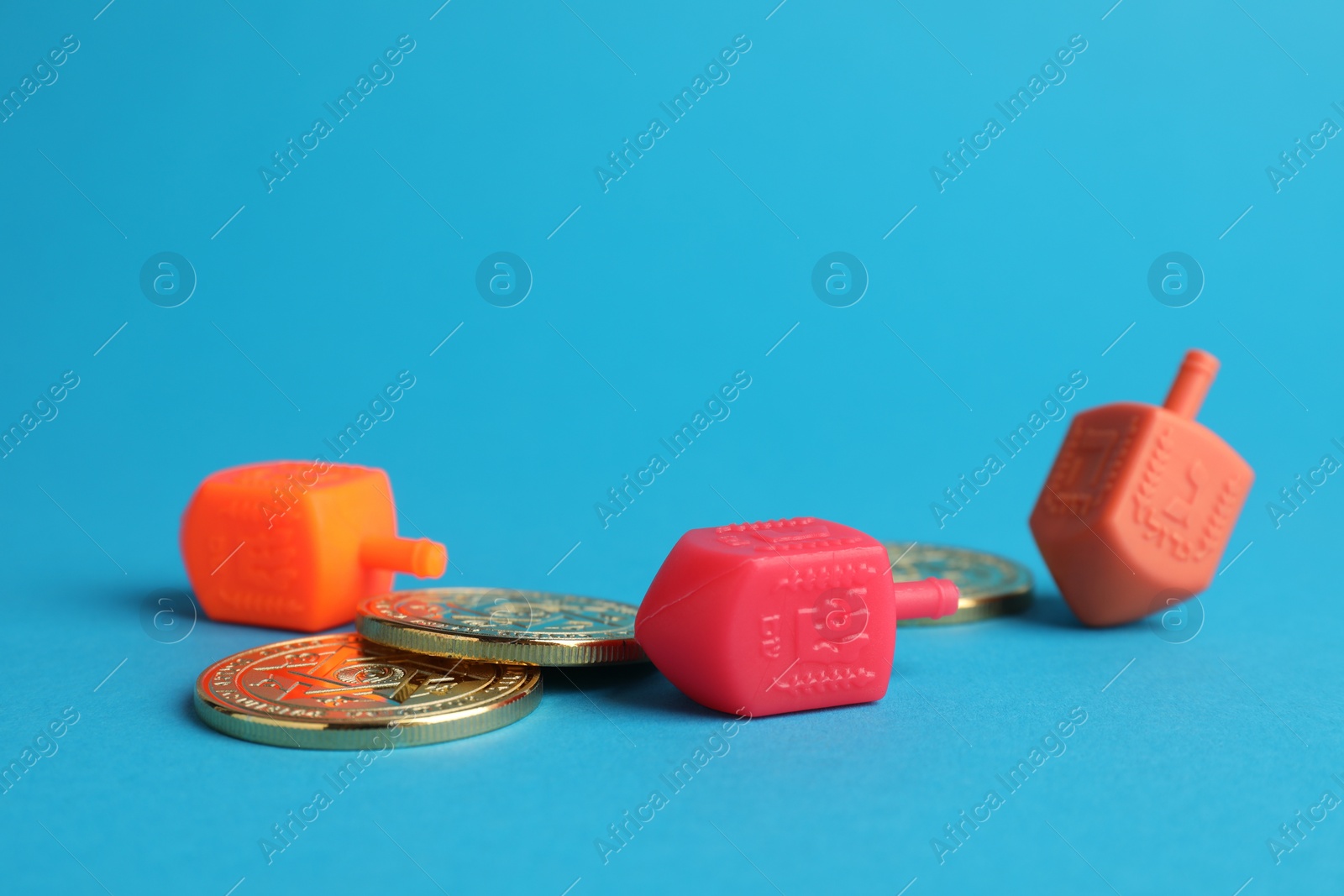 Photo of Dreidels with Jewish letters and coins on light blue background. Traditional Hanukkah game