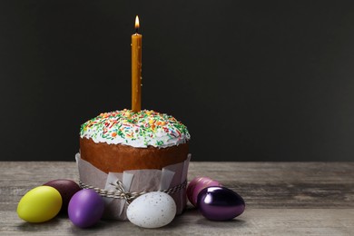 Traditional Easter cake with sprinkles, burning candle and painted eggs on wooden table, space for text