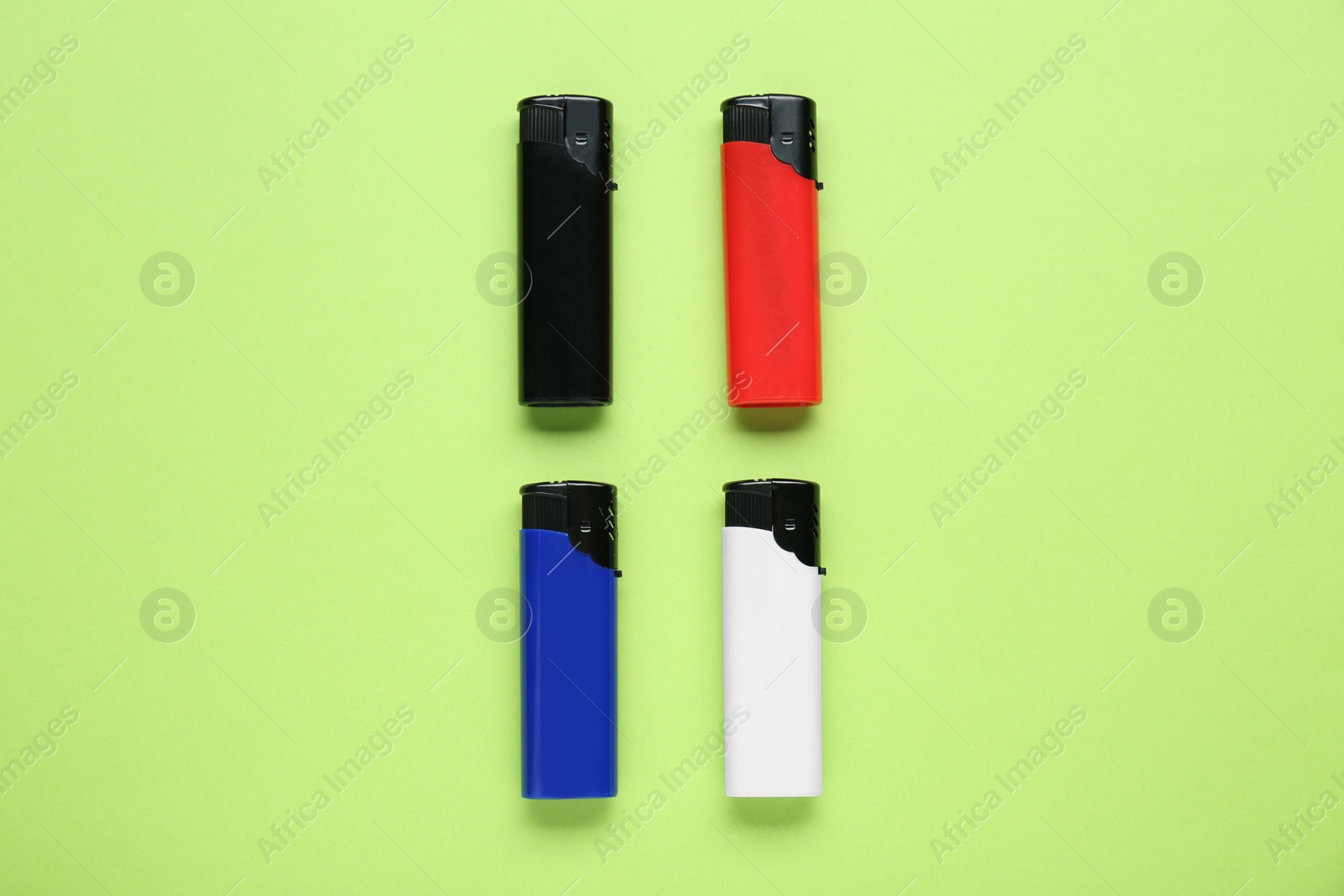 Photo of Stylish small pocket lighters on light green background, flat lay