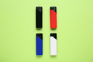 Photo of Stylish small pocket lighters on light green background, flat lay