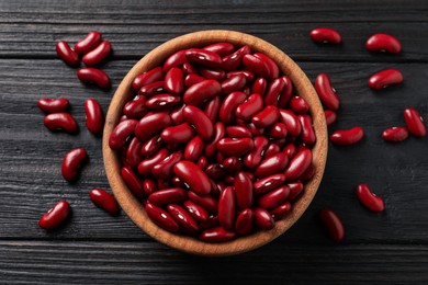 Photo of Raw red kidney beans and bowl on dark wooden table, flat lay