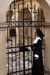 Photo of Young nun in cassock near metal door outdoors