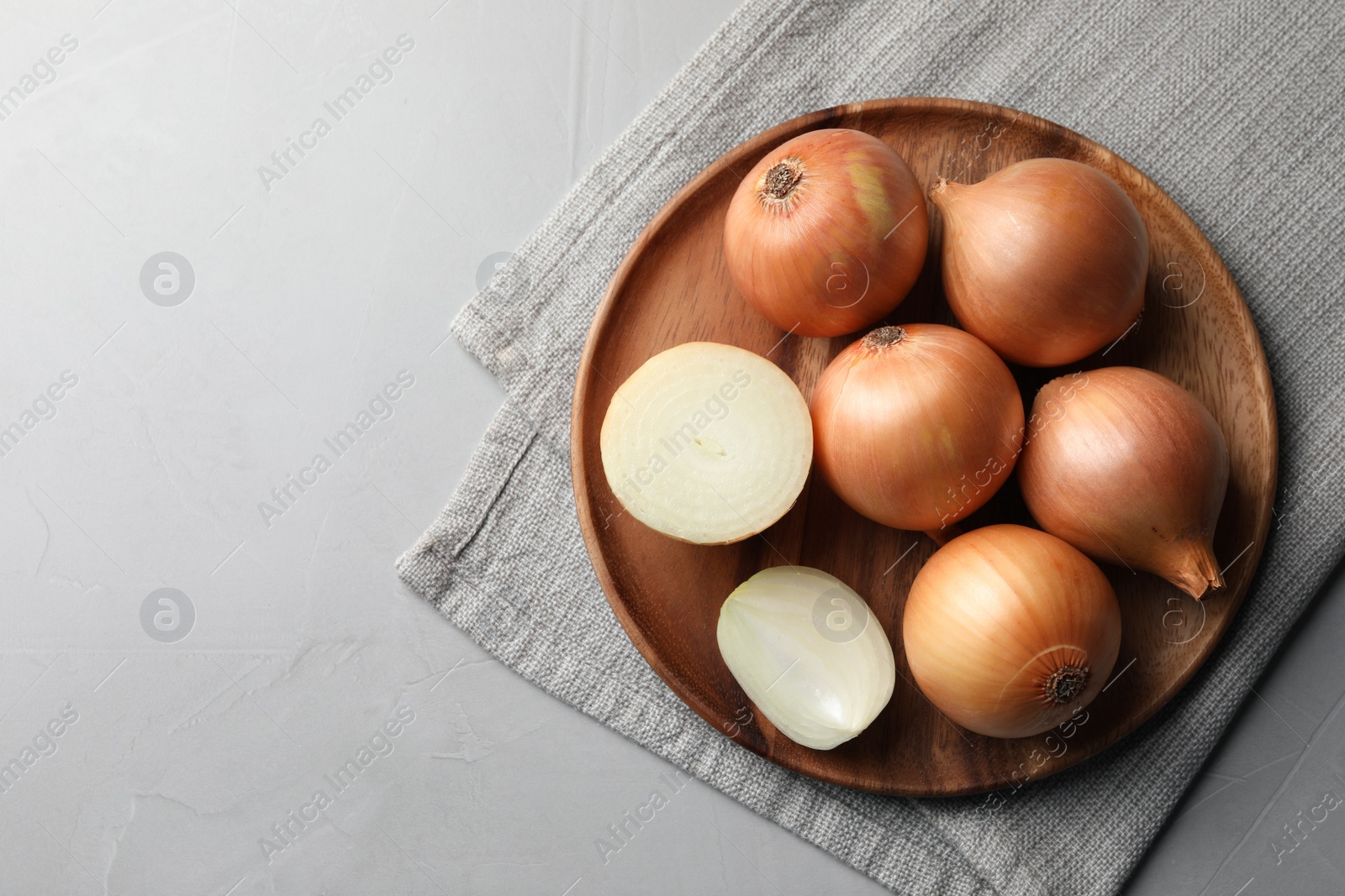 Photo of Whole and cut onions on light grey textured table, top view. Space for text