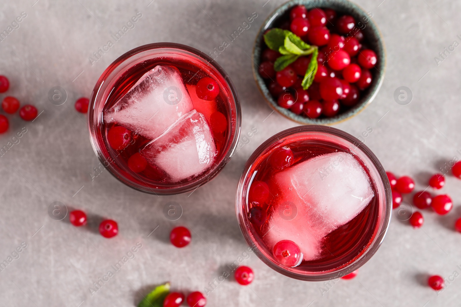 Photo of Tasty cranberry juice with ice cubes in glasses and fresh berries on light grey table, flat lay