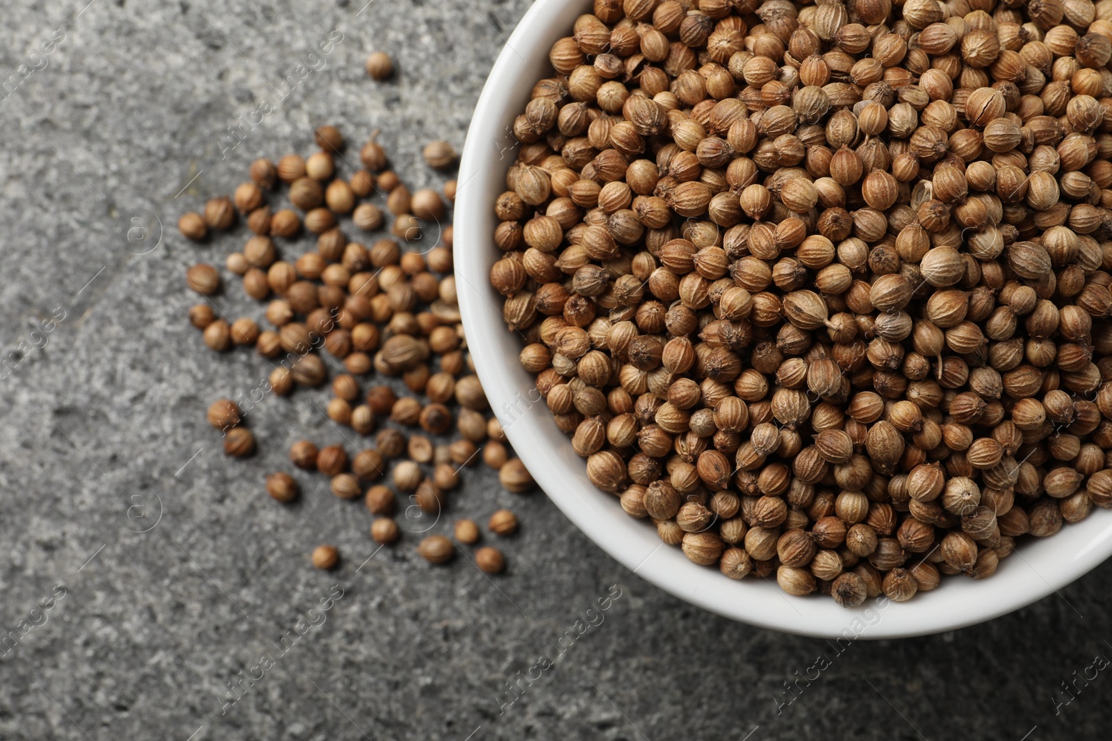 Photo of Dried coriander seeds in bowl on gray textured table, top view