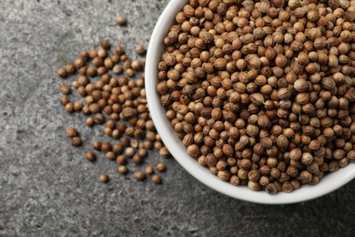 Dried coriander seeds in bowl on gray textured table, top view