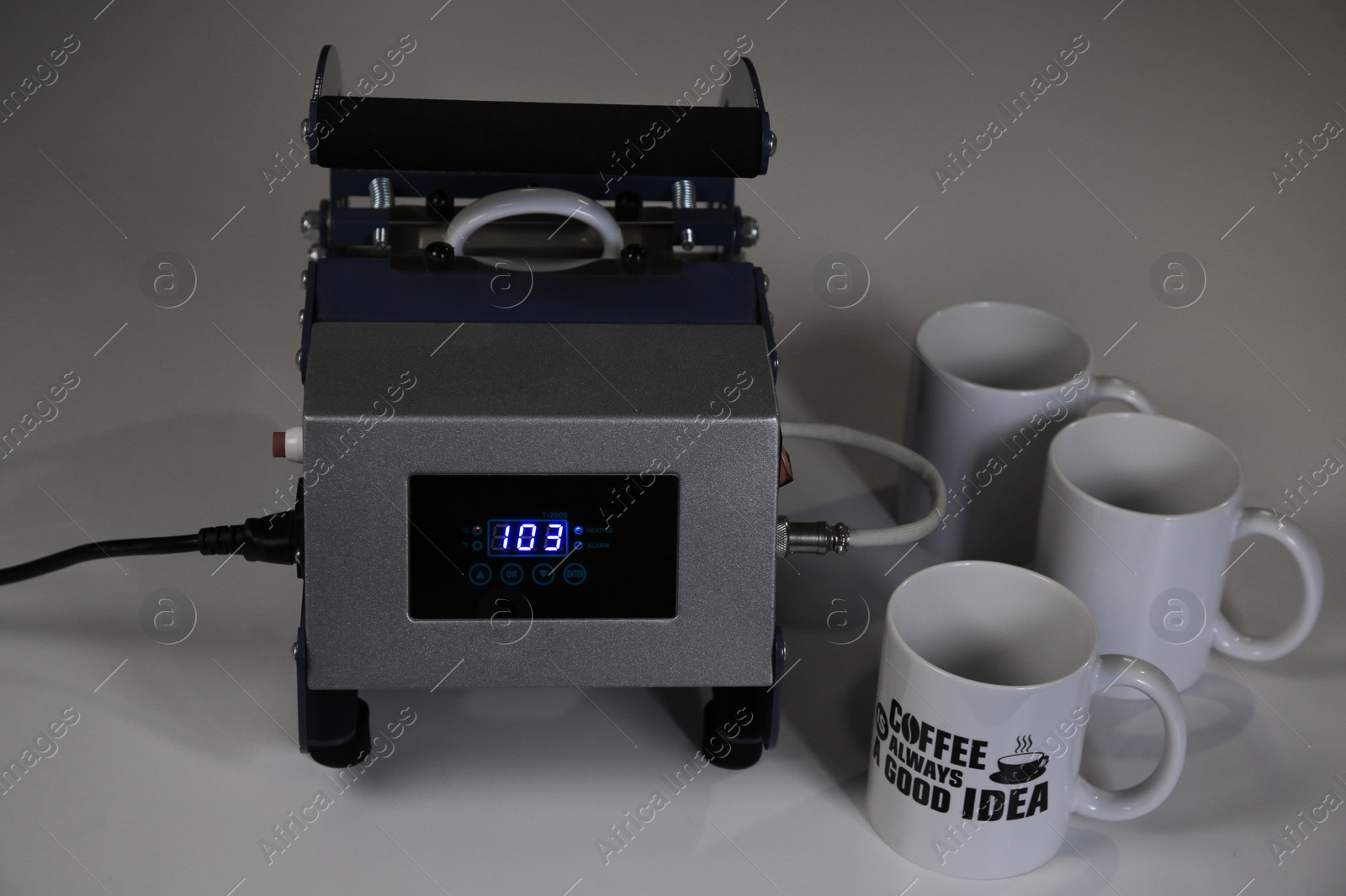 Photo of Printing logo. Heat press with cups on white table