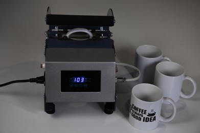 Printing logo. Heat press with cups on white table