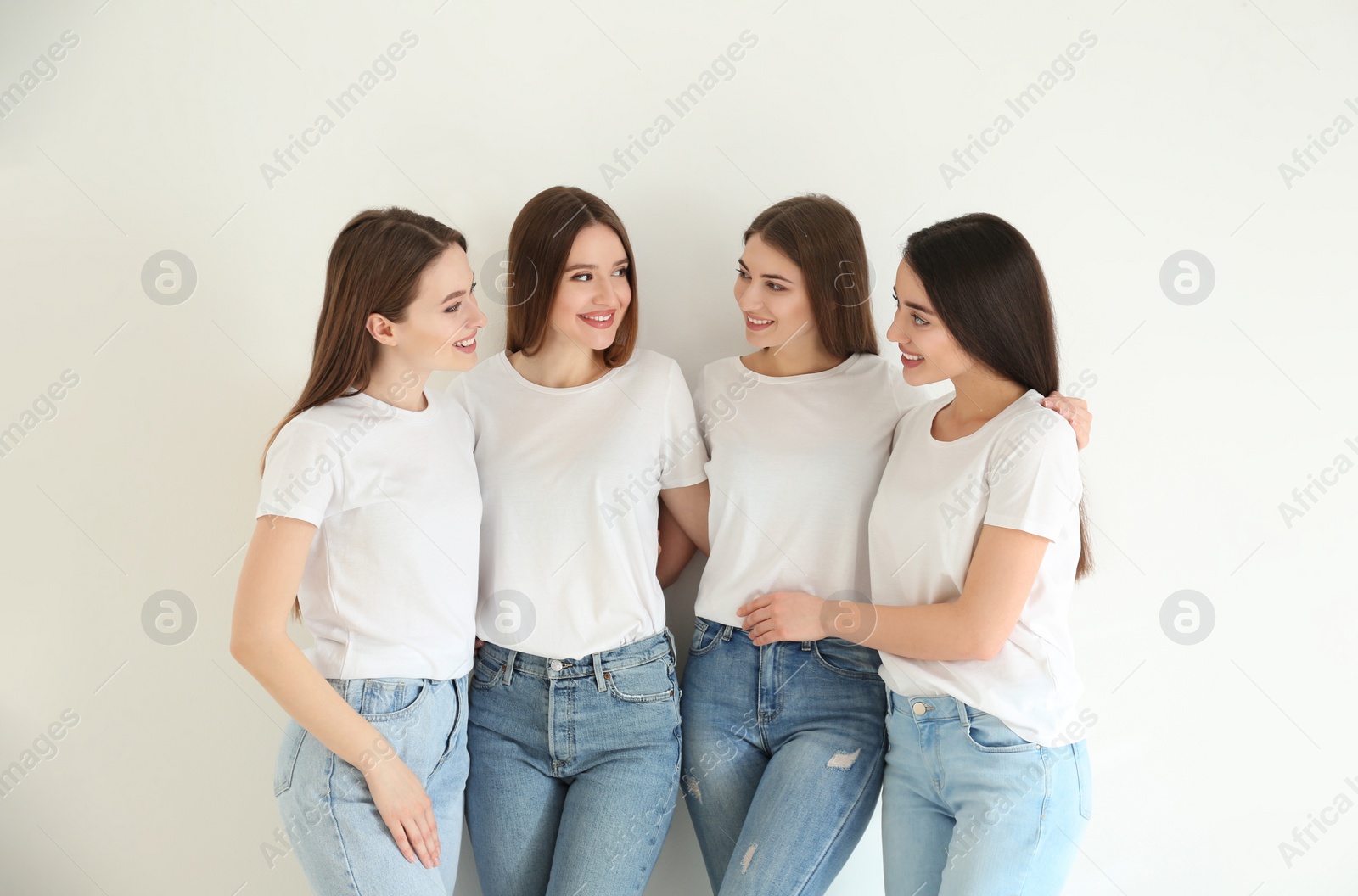 Photo of Beautiful young ladies in jeans and white t-shirts on light background. Woman's Day