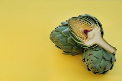 Cut and whole fresh raw artichokes on yellow background, closeup. Space for text