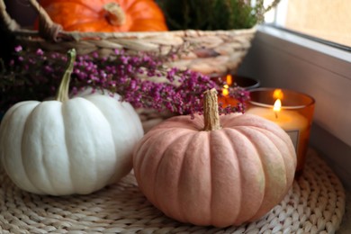 Photo of Wicker basket with beautiful heather flowers, pumpkins and burning candles near window indoors, closeup