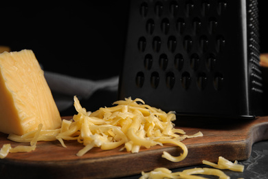 Delicious grated cheese on wooden board against black background