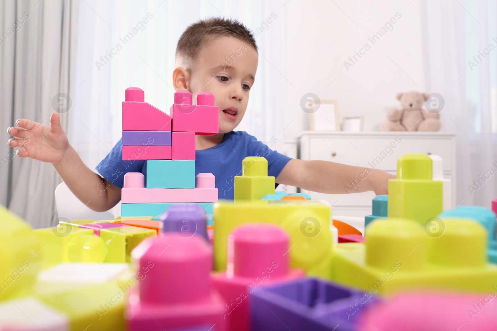 Photo of Cute little boy playing with colorful building blocks at table in room