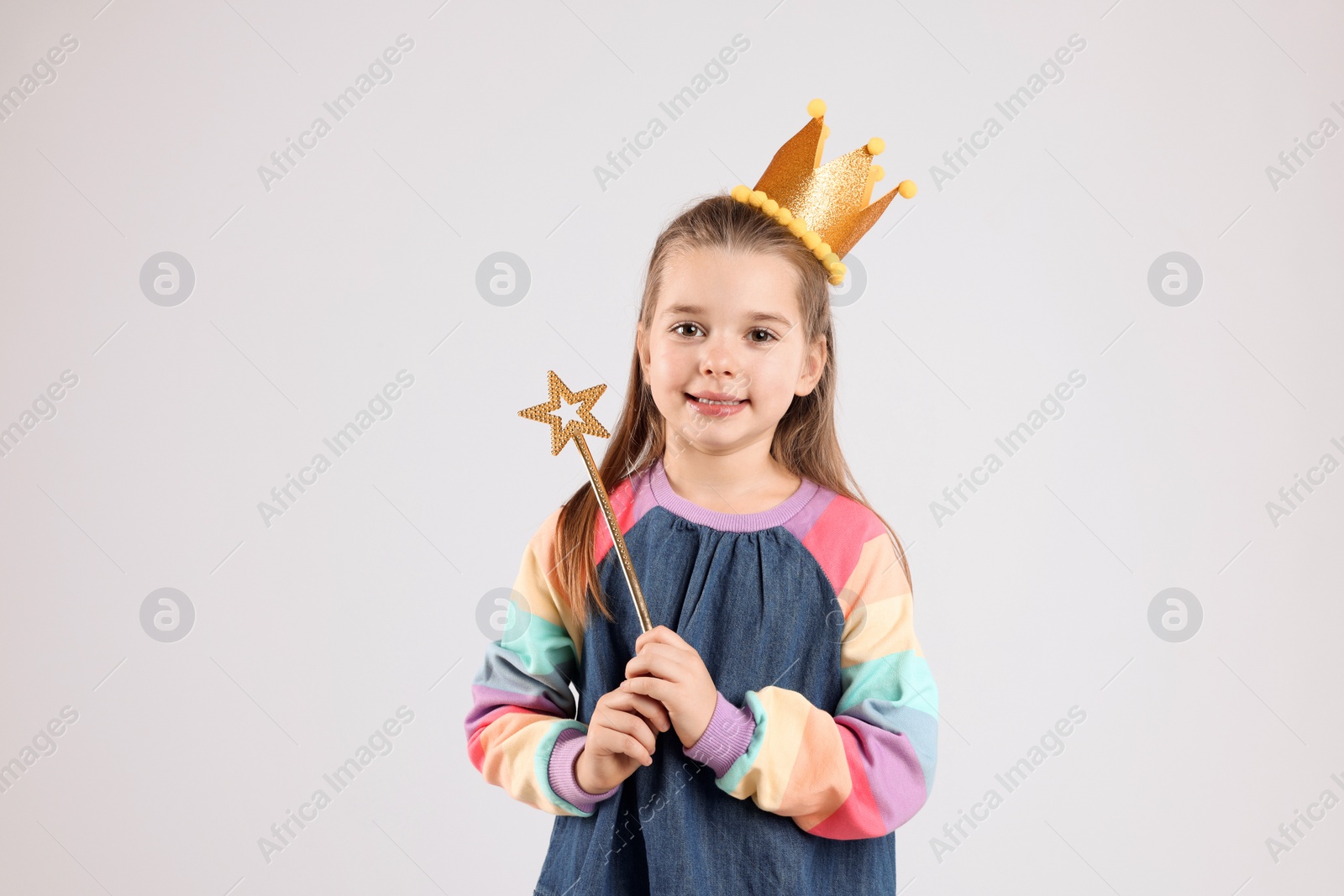 Photo of Cute girl in golden crown with magic wand on light grey background. Little princess