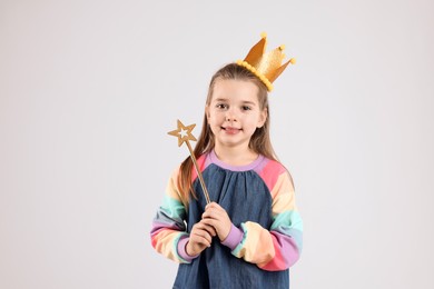 Cute girl in golden crown with magic wand on light grey background. Little princess