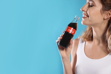 MYKOLAIV, UKRAINE - NOVEMBER 28, 2018: Young woman with bottle of Coca-Cola on color background, space for text