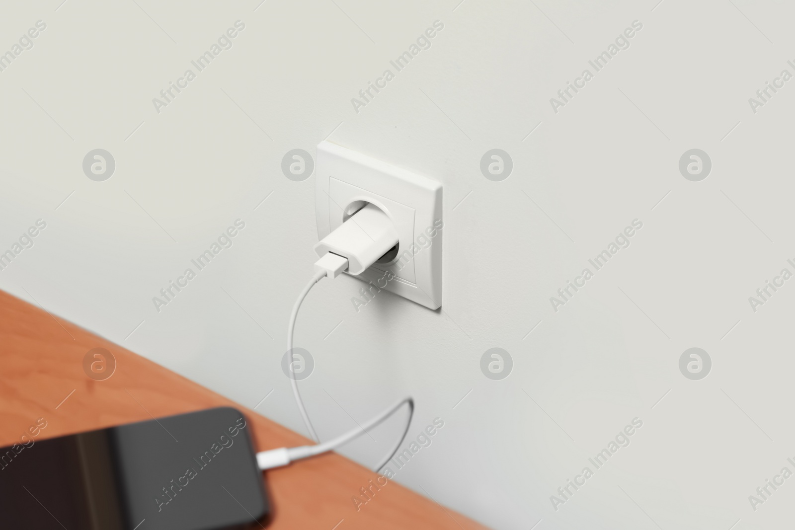 Photo of Modern smartphone charging from electric socket indoors