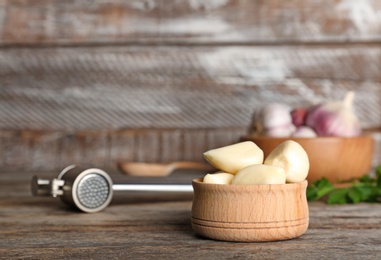 Photo of Garlic press and bowl with cloves on table