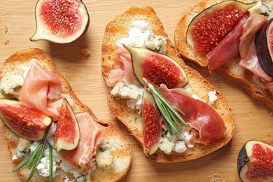 Photo of Bruschettas with cheese, prosciutto and figs served on wooden table, closeup