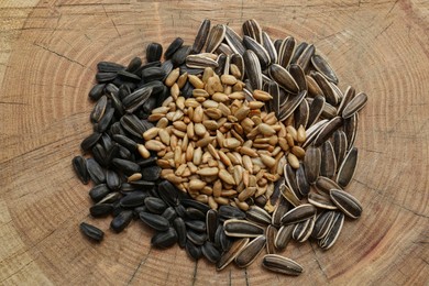 Photo of Pile of different sunflower seeds on wooden stump, top view