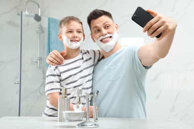 Photo of Son and dad with shaving foam on faces taking selfie in bathroom