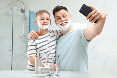 Son and dad with shaving foam on faces taking selfie in bathroom