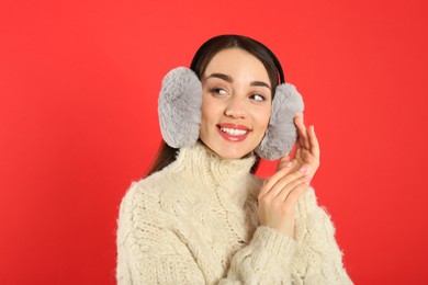 Photo of Beautiful young woman wearing earmuffs on red background