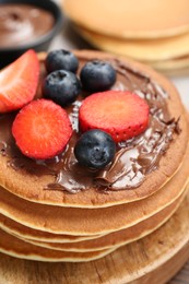 Photo of Tasty pancakes with chocolate paste and berries on table, closeup