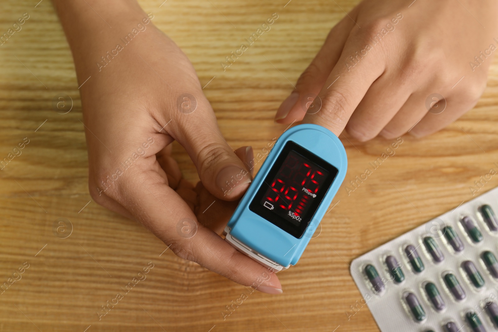 Photo of Man using pulse oximeter for oxygen level testing at wooden table, top view