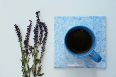 Cup of aromatic herbal tea and sage flowers on white table, flat lay