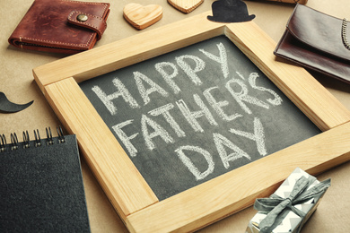 Photo of Chalkboard with phrase HAPPY FATHER'S DAY and male accessories on beige background, closeup