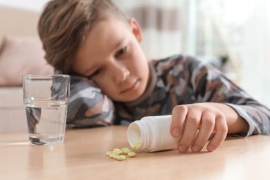 Photo of Little child with pills and water at table indoors. Danger of medicament intoxication
